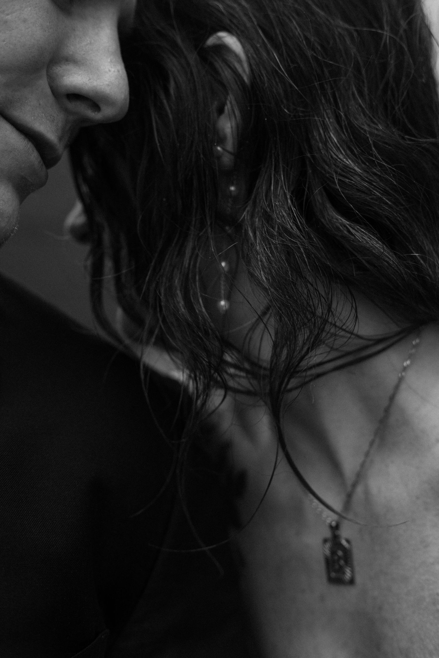 Close-up black and white photo of long dark hair and a delicate necklace pendant.