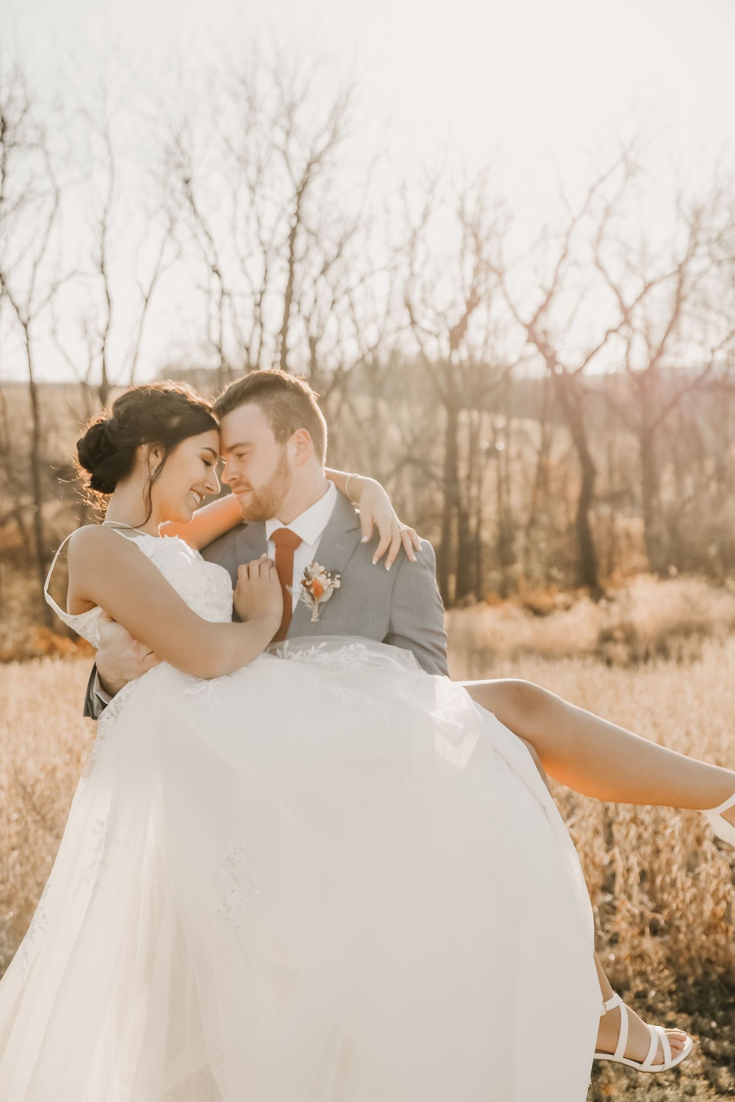 Romantic wedding photo of couple in sunlit field with groom carrying bride.