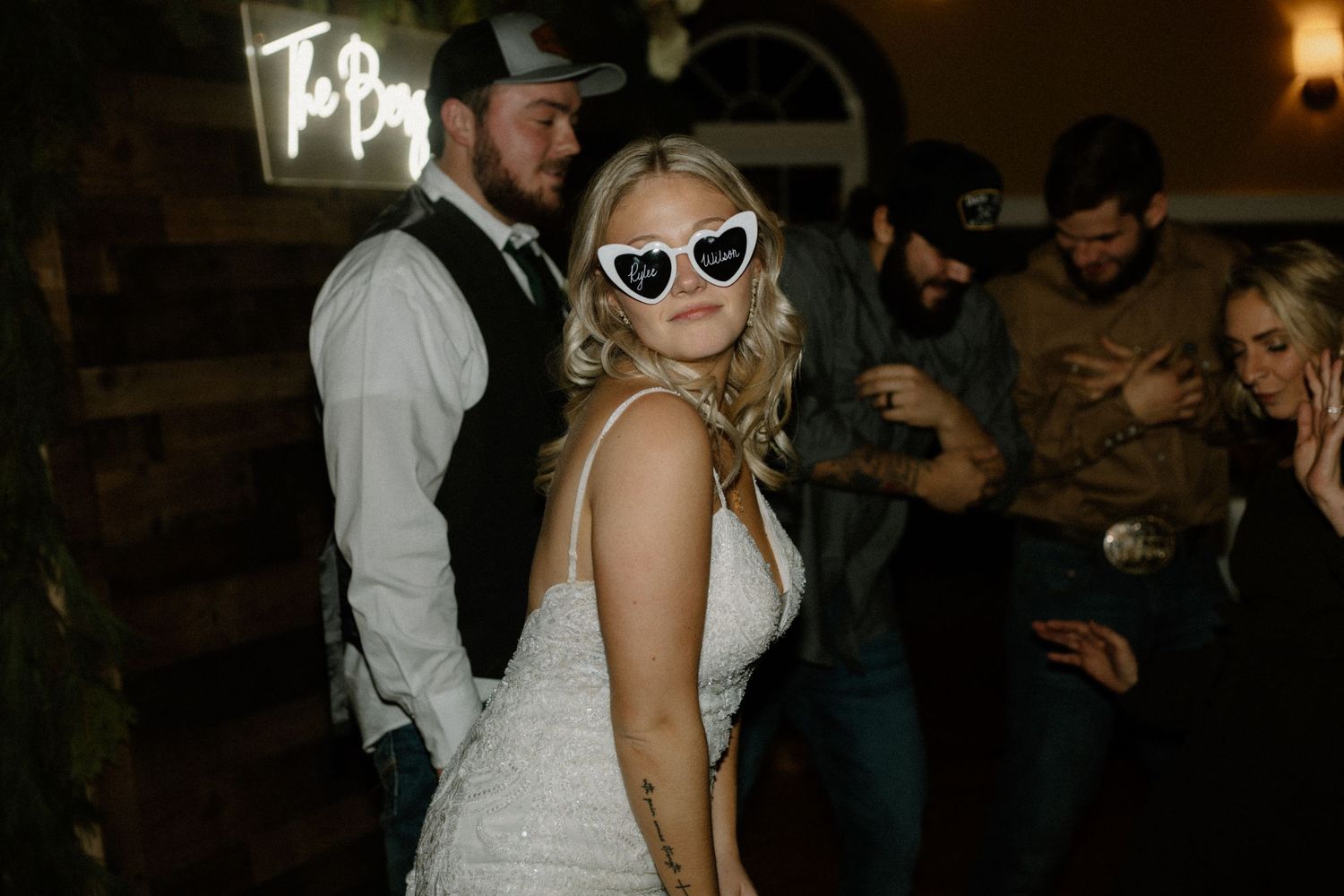 Wedding reception scene with retro sunglasses and neon sign in background.