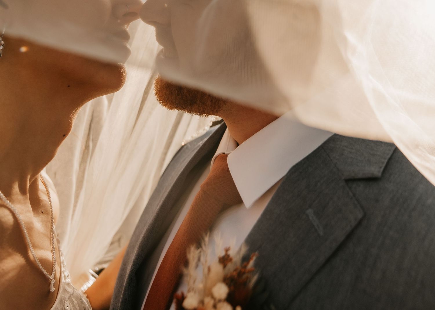 Close up detail of formal wedding attire showing suit jacket, boutonniere and white dress.