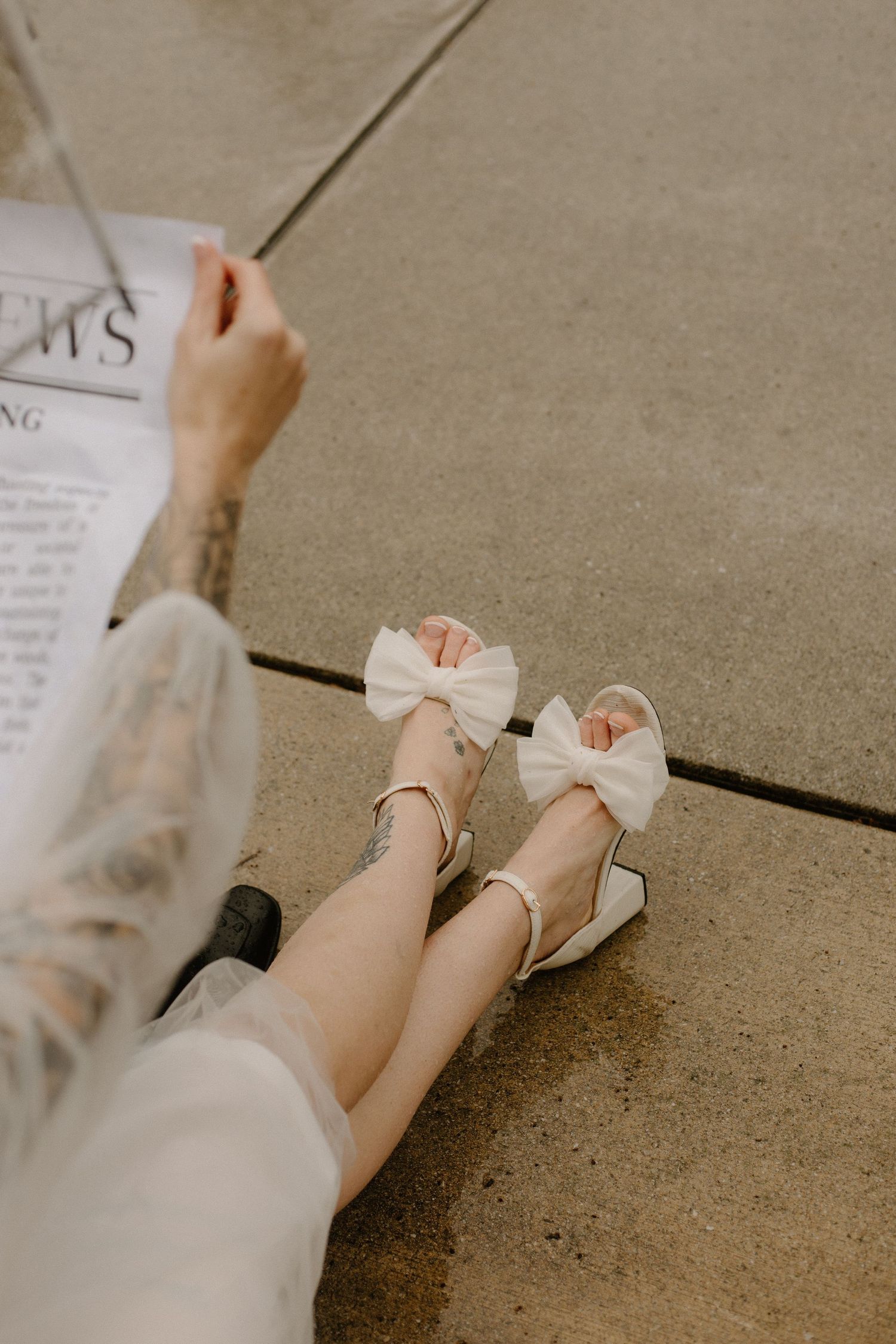 White bow shoes and newspaper on concrete floor in soft vintage tones.