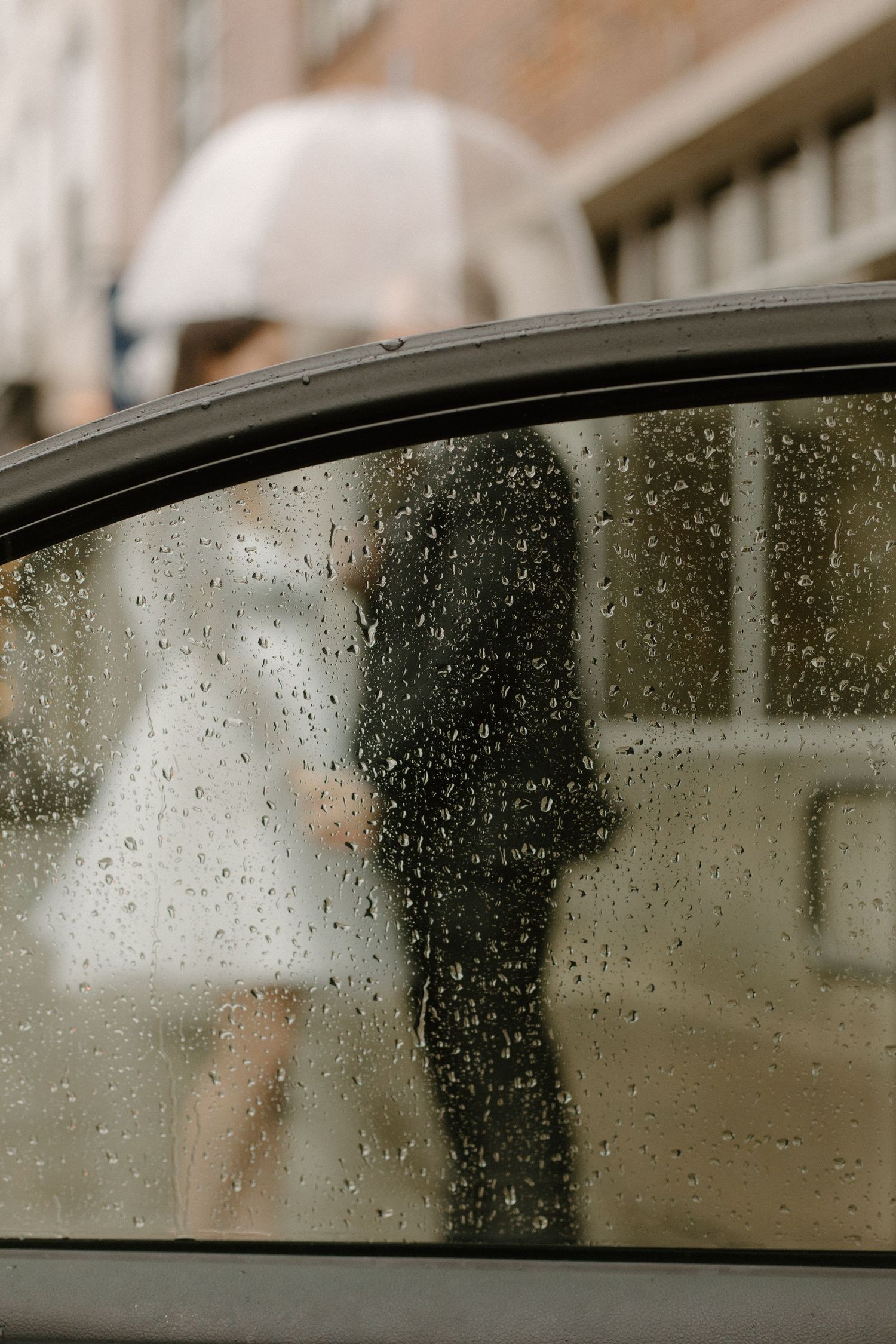 Rain drops on a car window with a silhouetted couple visible through the glass.