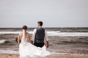 Couple looking out at stormy ocean on beach in formal wedding attire.