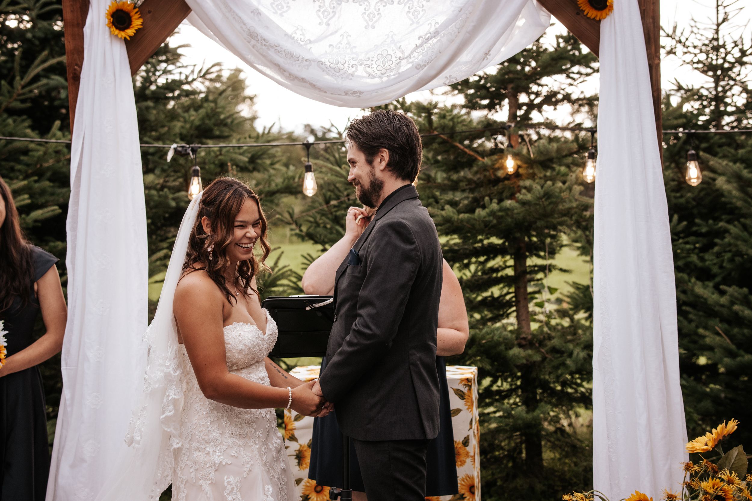 Couple exchanging vows under white draped arch during outdoor wedding ceremony.