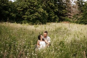 A romantic moment captured in a sunlit meadow filled with tall wildflowers and surrounded by trees.