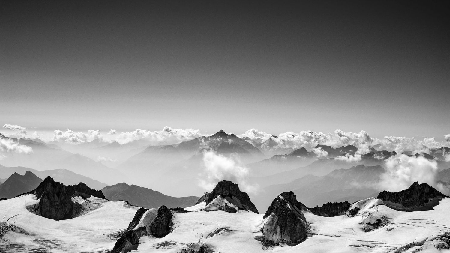Dramatic black and white landscape of snow-covered mountain peaks rising above clouds.