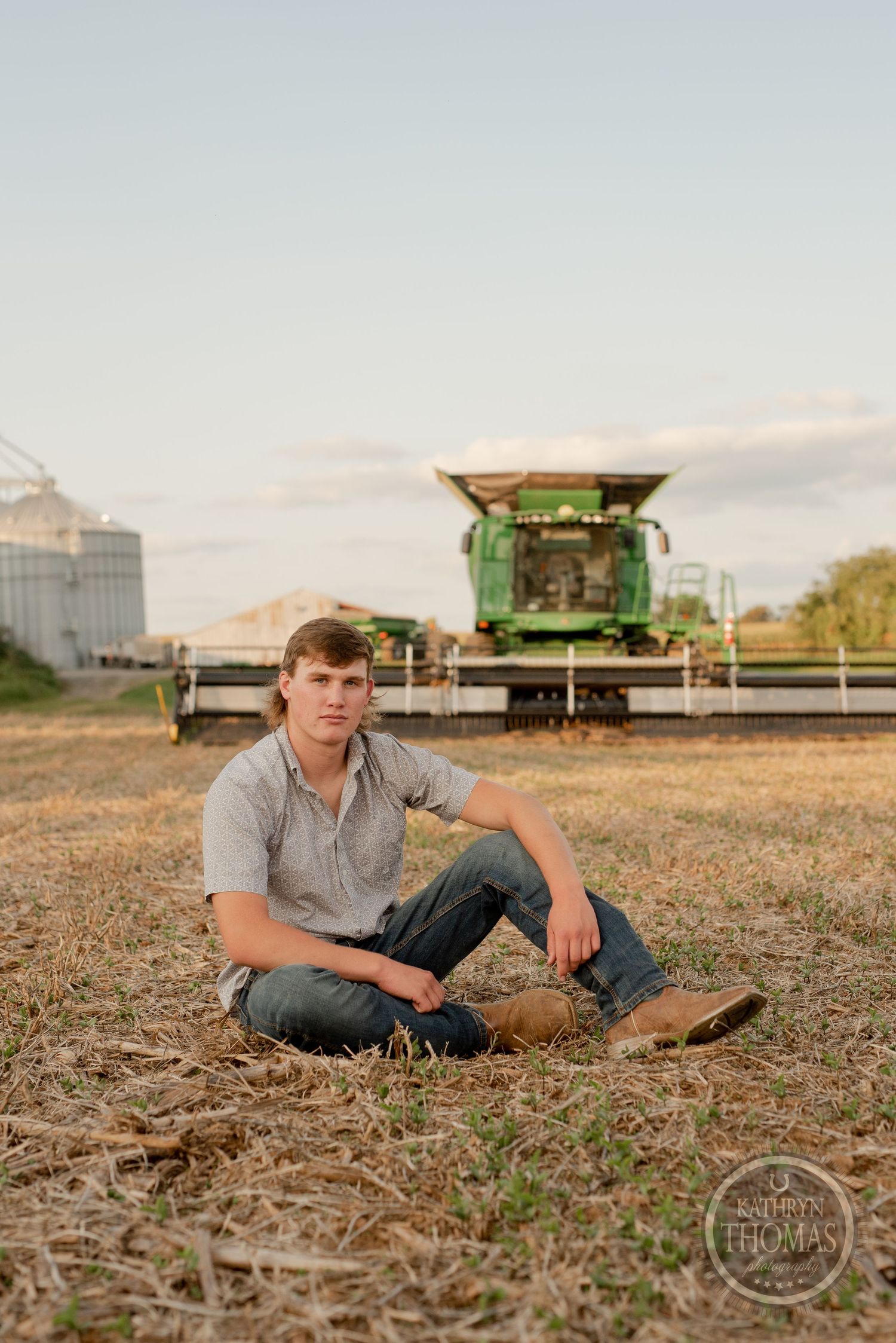 Farm scene with large green combine harvester and grain storage facilities in background.