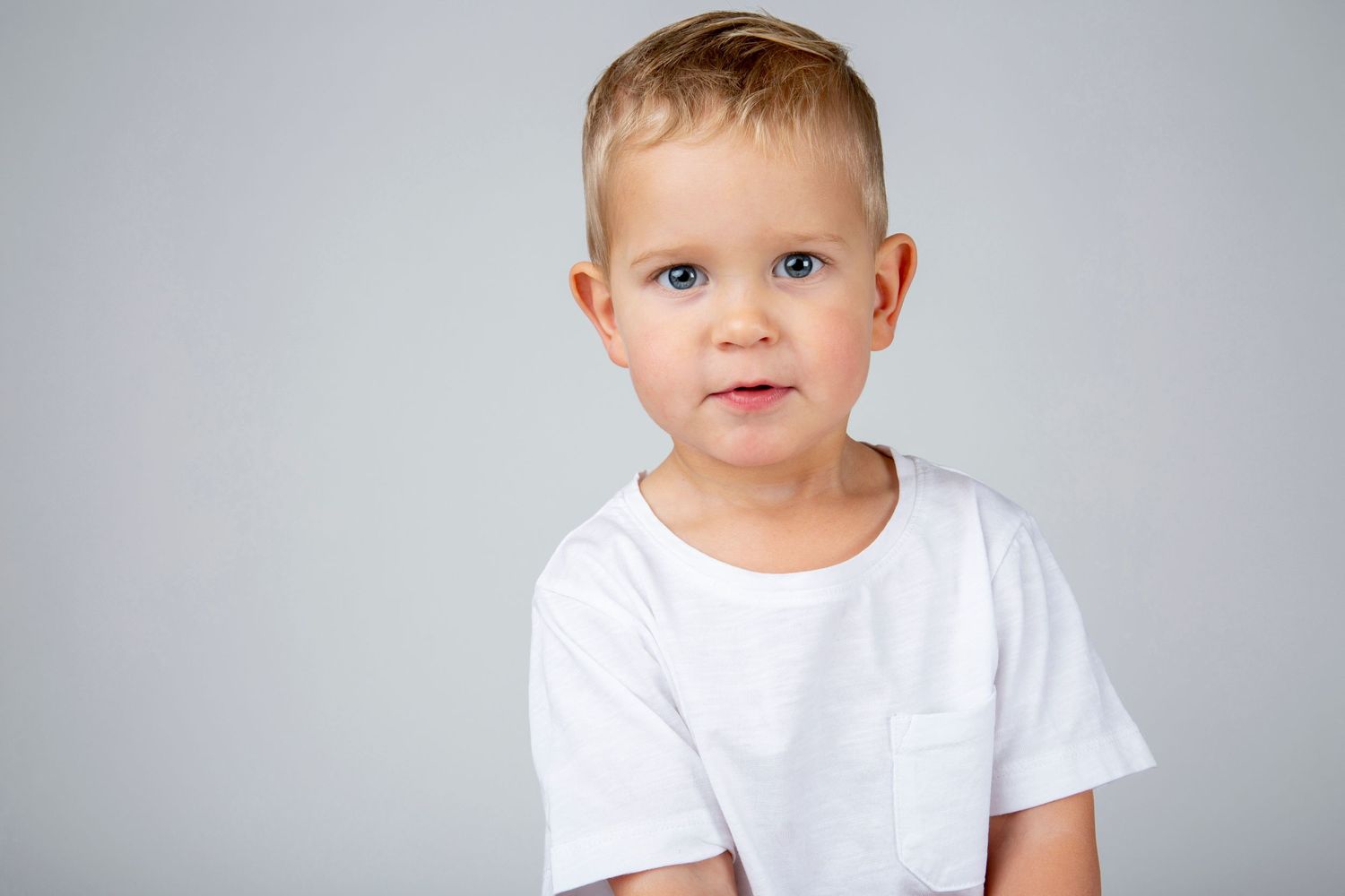 A young child in a white t-shirt poses against a grey background.