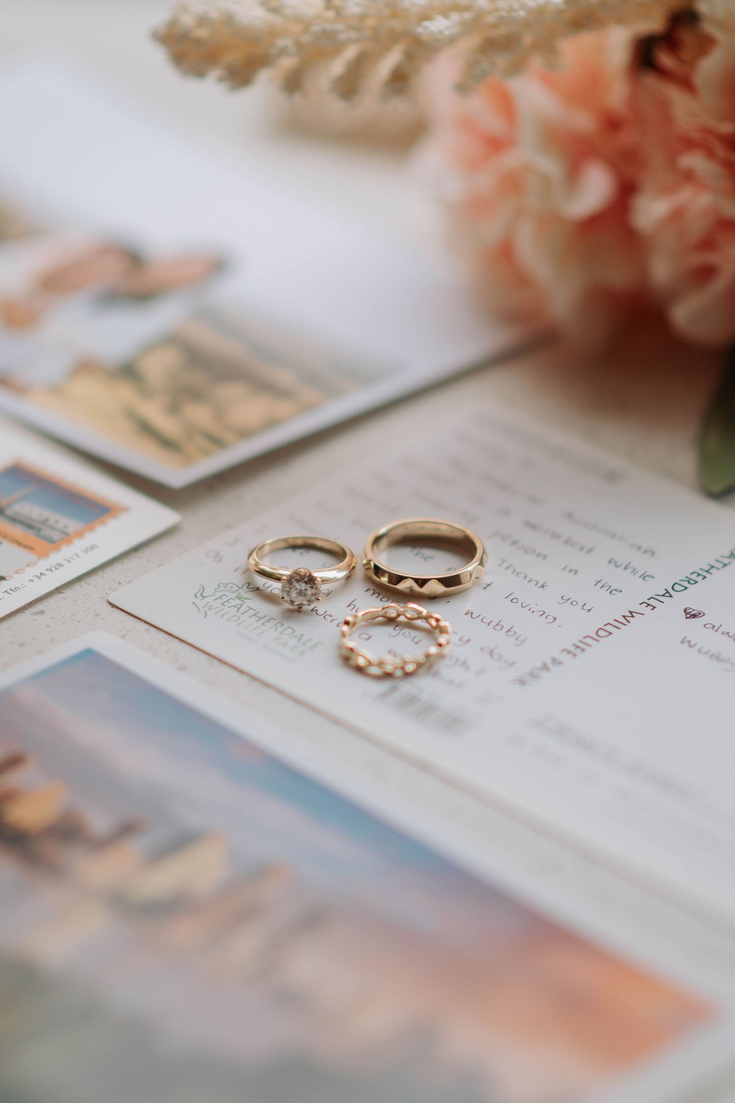 Three wedding rings arranged on paper with blurred flowers in soft peach colors in the background.