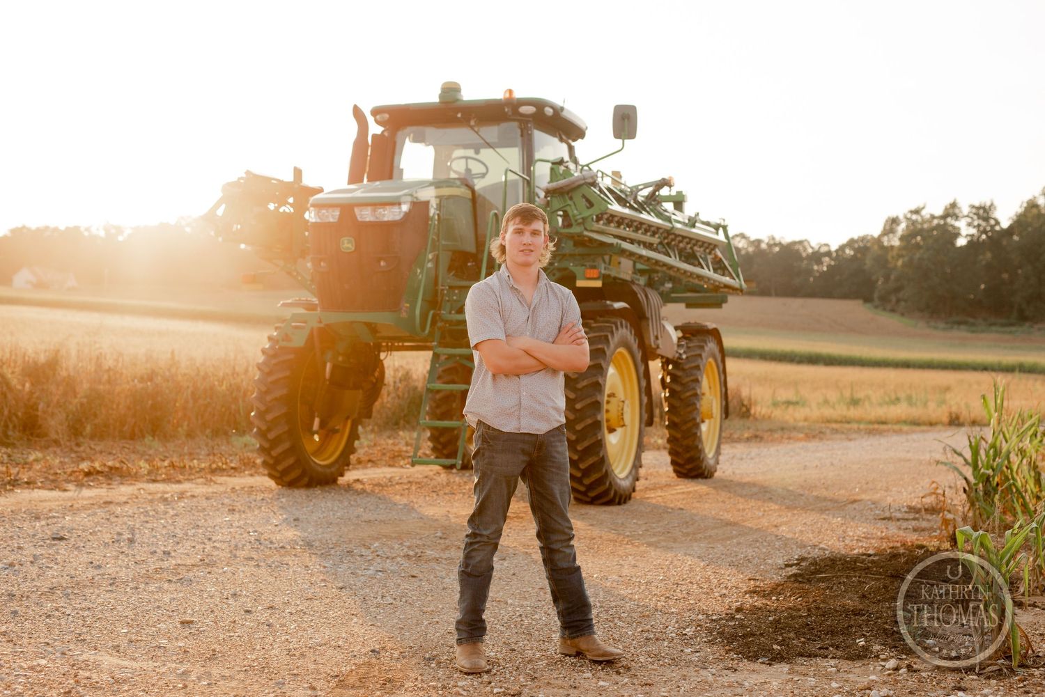 Silhouette of a farmer standing in front of a large John Deere tractor during golden hour.