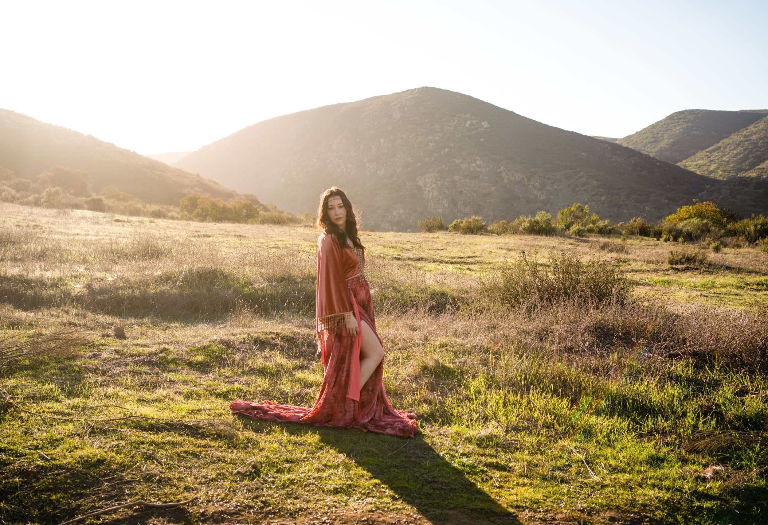 A flowing red dress catches golden sunlight in a serene mountain meadow during sunset.