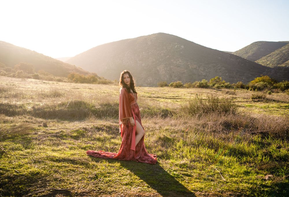 A flowing red dress catches golden sunlight in a serene mountain meadow during sunset.
