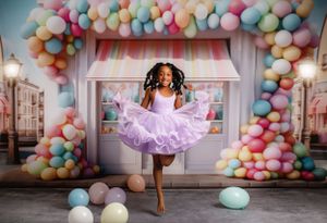 Young dancer twirls joyfully in a purple tutu dress against a pastel balloon arch and pink storefront backdrop.