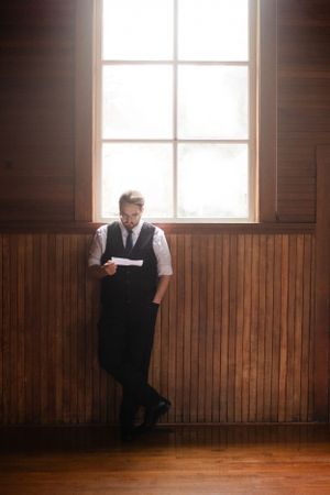 A person in formal attire reading by a sunlit window in a wood-paneled room.