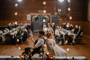 Wedding reception scene in a rustic wood-paneled hall with hanging lights and celebrating guests.