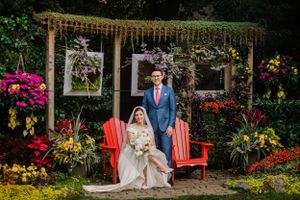 Wedding ceremony setup in vibrant garden with red chairs and floral arch featuring hanging decor and colorful flowers.