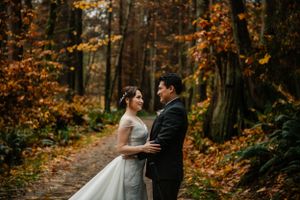 Newlyweds share an intimate moment on a forest path covered in autumn leaves.