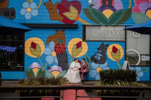 Couple posing against colorful floral mural wall outside a store.