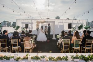 A rooftop wedding ceremony with string lights and white decor against an urban backdrop.