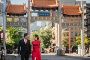 Couple walking through Chinatown gate with traditional red and gold architecture in urban setting.