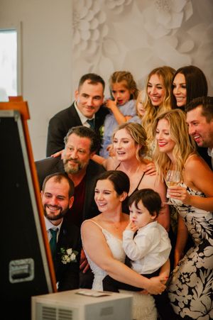 Wedding celebration group gathered around photo booth with joyful expressions.