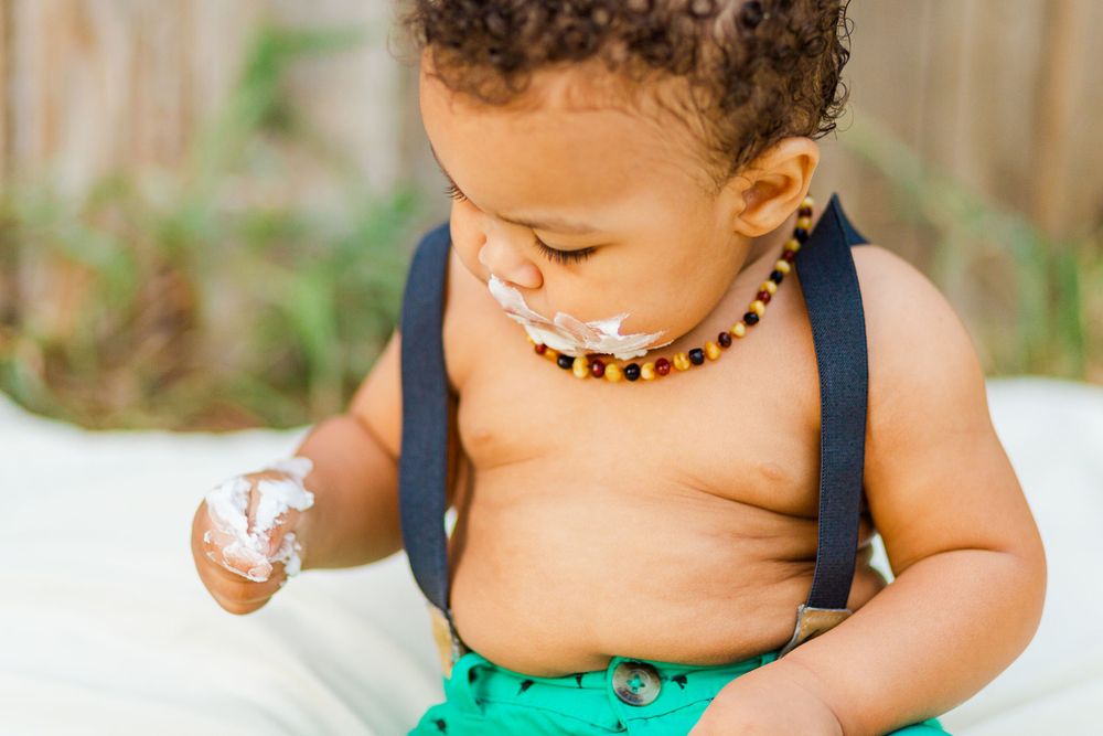 Toddler in suspenders and beaded necklace looking down during outdoor portrait session.