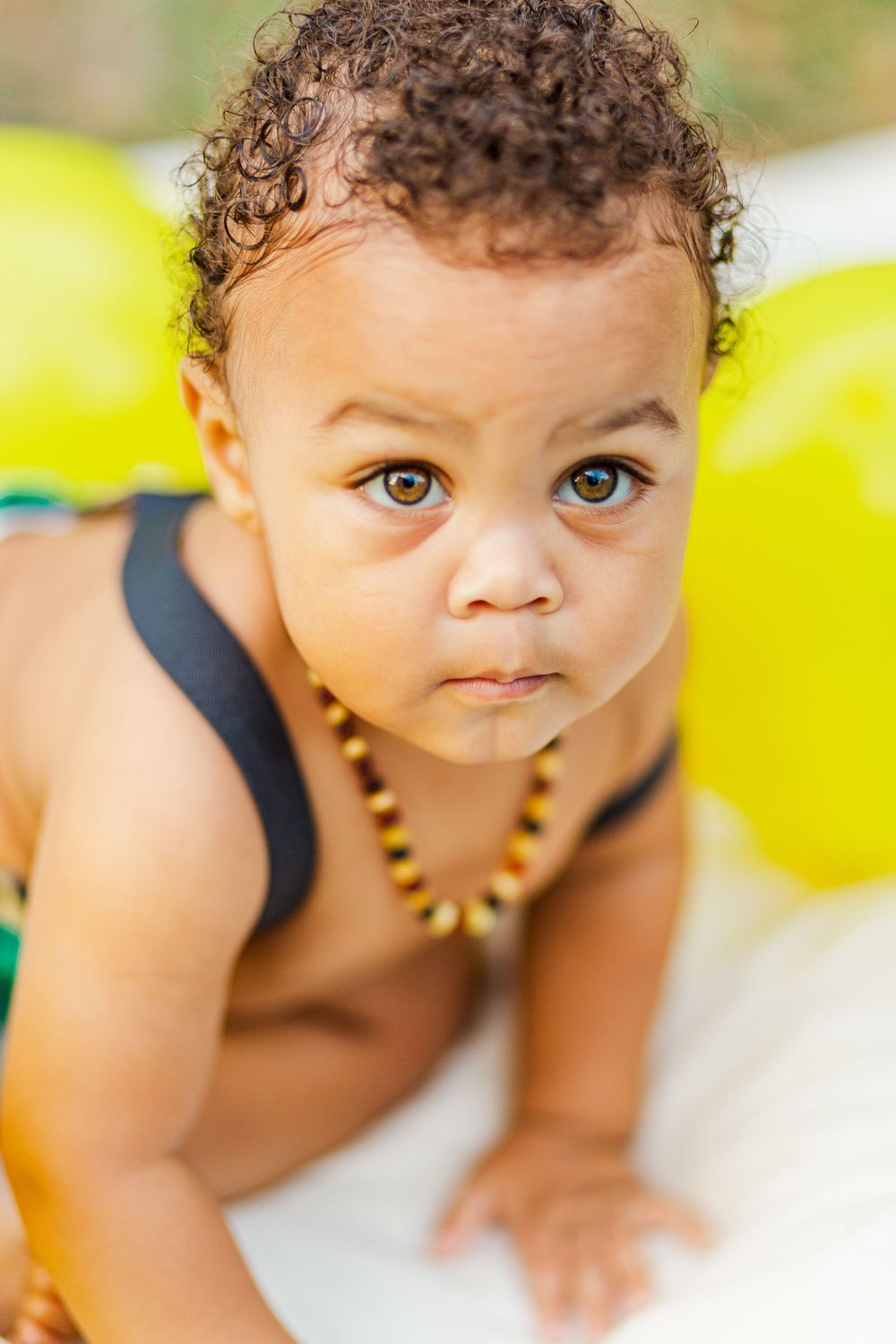 Adorable toddler with curly hair wearing beaded necklace during outdoor photo session.