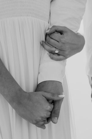 Close-up of hands adjusting a white dress sleeve showing an engagement ring.