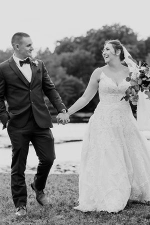 Black and white photo of laughing newlyweds walking hand in hand outdoors.
