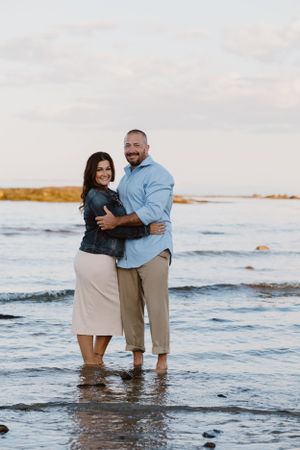 Couple embracing while standing in shallow ocean water at sunset.