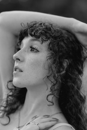 Black and white profile portrait of a woman with curly hair looking upward with hand raised.