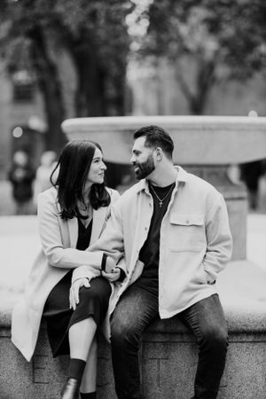 A loving couple shares an intimate moment while sitting on a stone wall in a park setting.