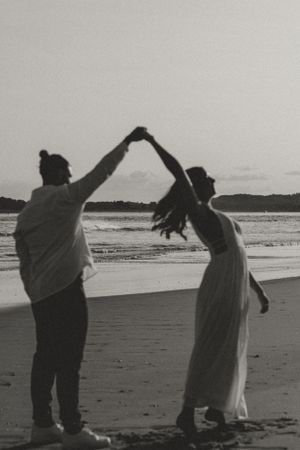 Couple dancing and twirling on beach in black and white.