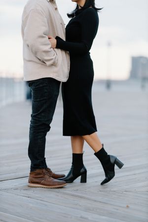 A close-up of a couple's coordinated outfits and shoes while standing on a wooden deck.