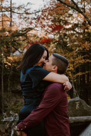 A couple sharing an intimate moment surrounded by vibrant fall trees at sunset.