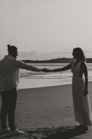Silhouette of couple holding hands on beach during sunset.