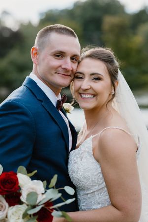 Happy bride and groom smile together while holding red and white wedding bouquet.