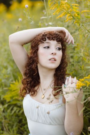A dreamy portrait of a woman in white among yellow wildflowers with natural curly hair.