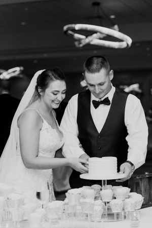 A couple in wedding attire cutting their wedding cake together at their reception.