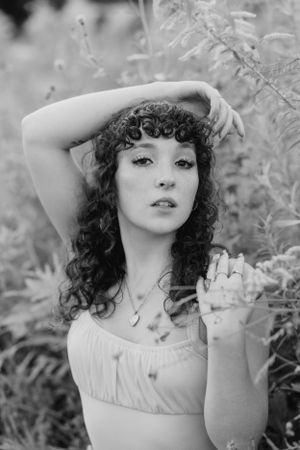 Artistic black and white portrait of a woman with curly hair in a white top among foliage.