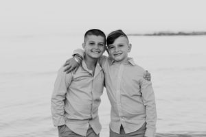 Two young boys in matching gray shirts stand together near a waterfront in a black and white photo.