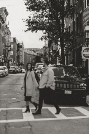 A black and white street scene showing a couple crossing an urban intersection.