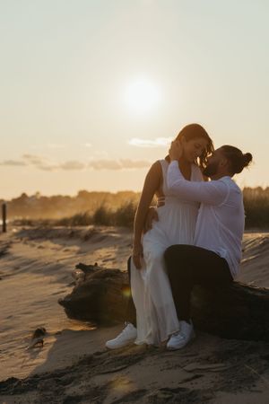 Romantic couple embrace on beach rocks during golden sunset.