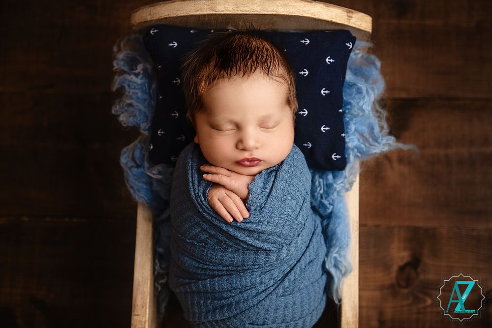Newborn photography featuring baby in blue wrap against navy starry background.