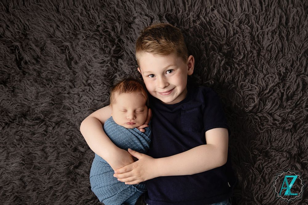 Two children cuddling on brown fuzzy blanket during professional portrait session.