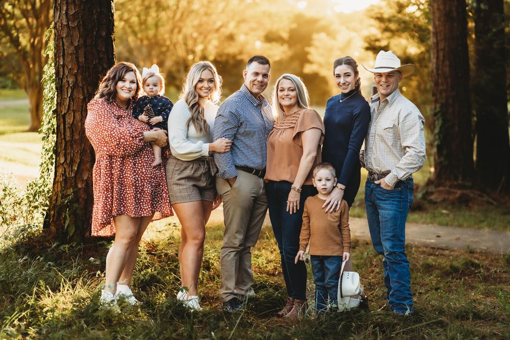 A large extended family poses together for a casual outdoor portrait at sunset among trees.