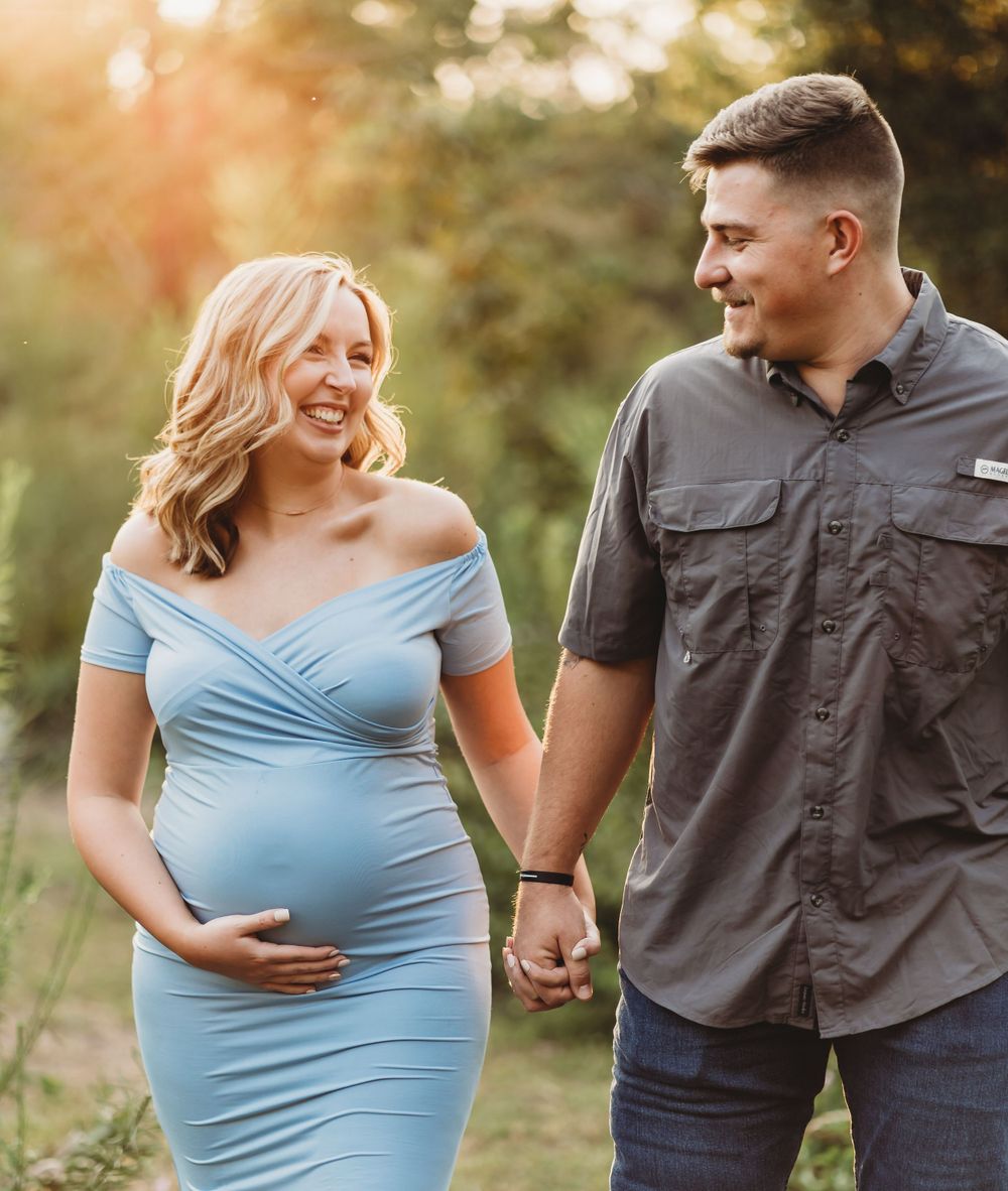 Couple walking hand in hand outdoors, woman wearing flowing blue maternity dress.
