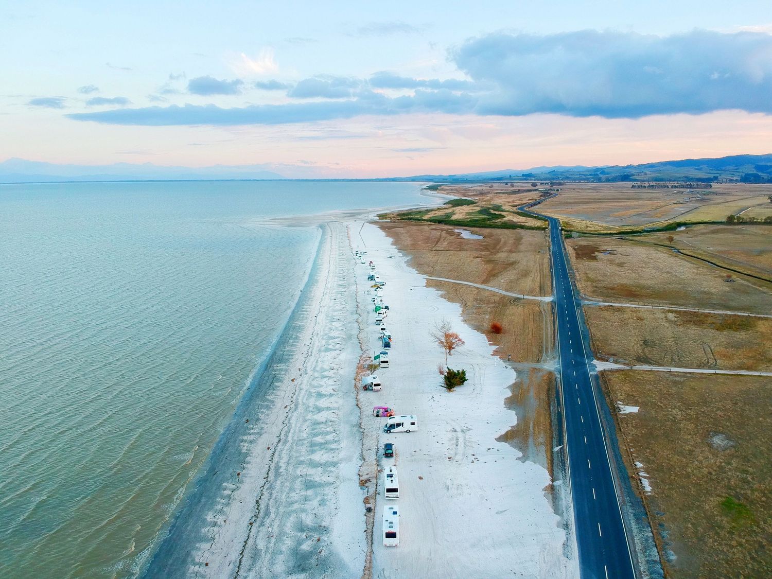 Aerial view of coastal highway along beach with parked cars and ocean.
