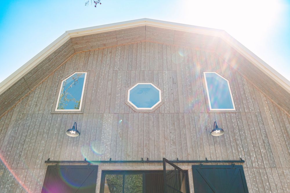 Modern wooden barn venue exterior with geometric windows against bright blue sky.