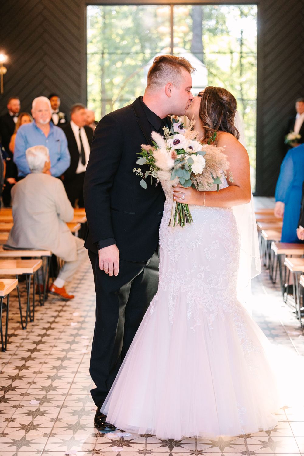 First kiss as newlyweds in chapel with guests seated behind.